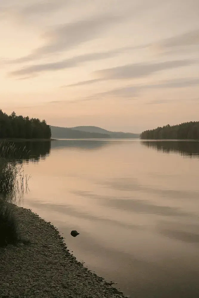 Rauhallinen järvimaisema auringonlaskun aikaan, tyyni vesi ja pehmeät pastellinsävyt luovat seesteisen ja meditatiivisen tunnelman.