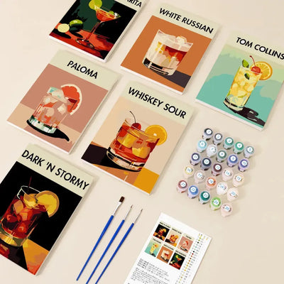 Classic Cocktails -numeromaalaussetti, jossa kuusi 20x15 cm drinkkiteemaista maalausta nimillä, maalipurkit, pensselit ja ohjeet pöydälle aseteltuna.