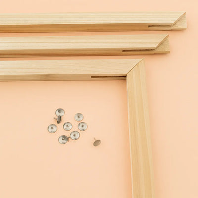 Puinen 40x50 cm paint by numbers -kiilakehys ennen kokoamista. Neljä puupalaa ja metalliset kiinnitysnastat on aseteltu vaalealle taustalle, valmiina kehyksen kasausta varten.