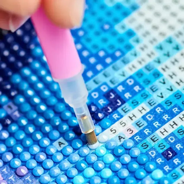 Timantteja asetellaan kankaalle kynällä symboleiden mukaan